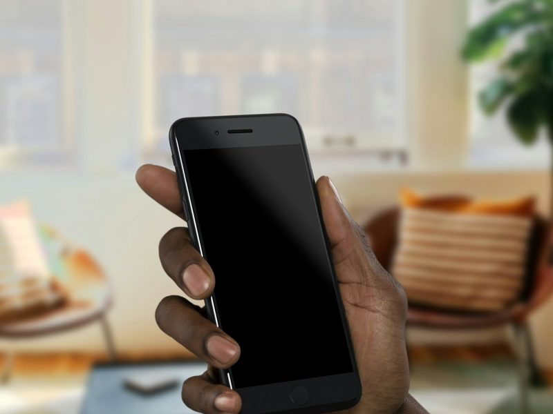 A hand holding a phone in a sunlit living room.