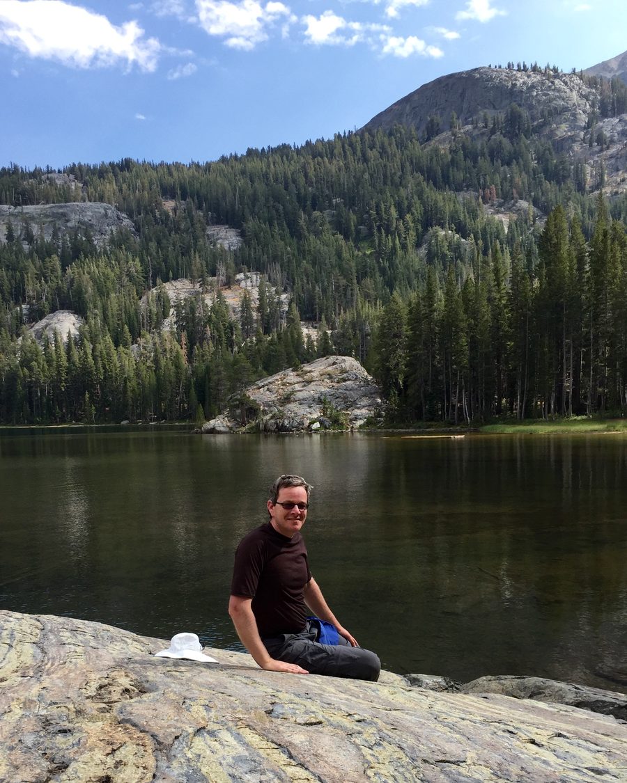 Jonathan Bricker seated on granite beside an alpine lake.